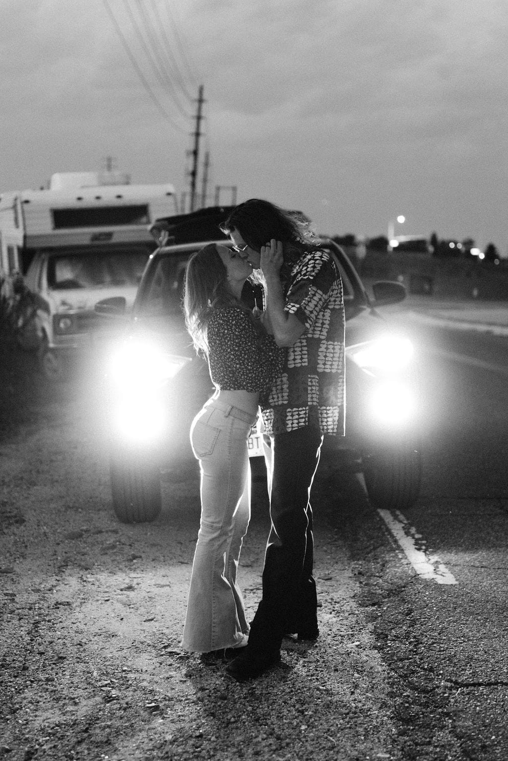 Couple kisses romantically at their denver colorado engagement session in front of their car headlights