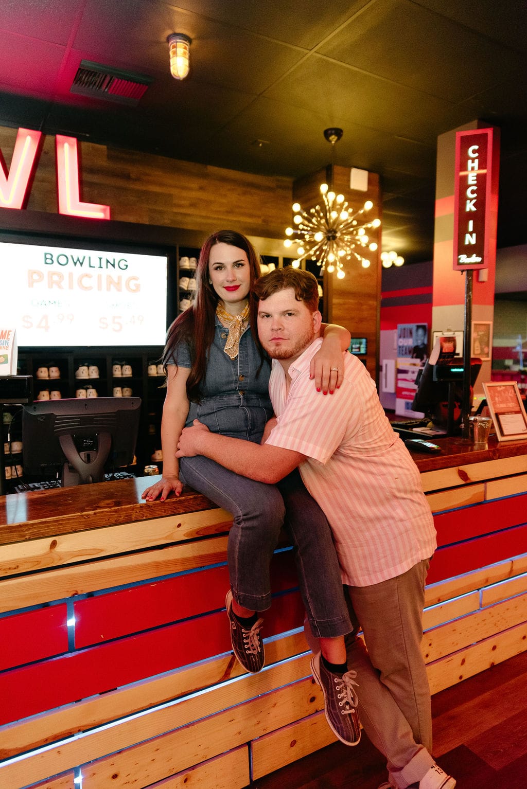 Couple sits on counter at bowling alley during their engagement session