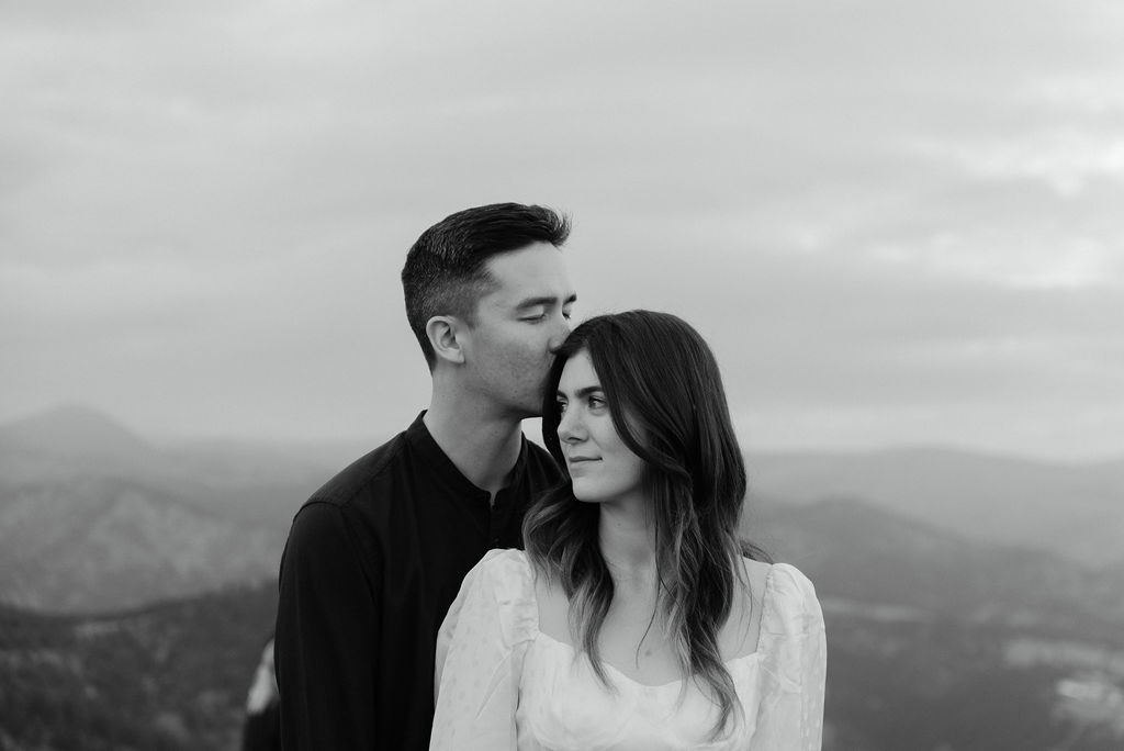 Dreamy Couples Portrait where boy kisses girls cheek on top of mountain