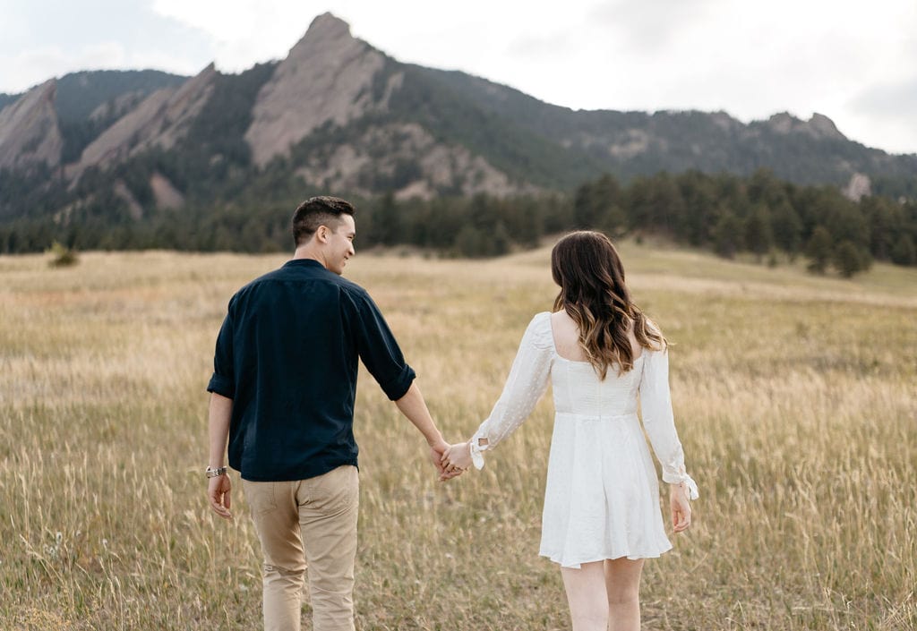 Mountain Engagement photos taken in Boulder Colorado walking through a field at Chautauqua Park hand in hand