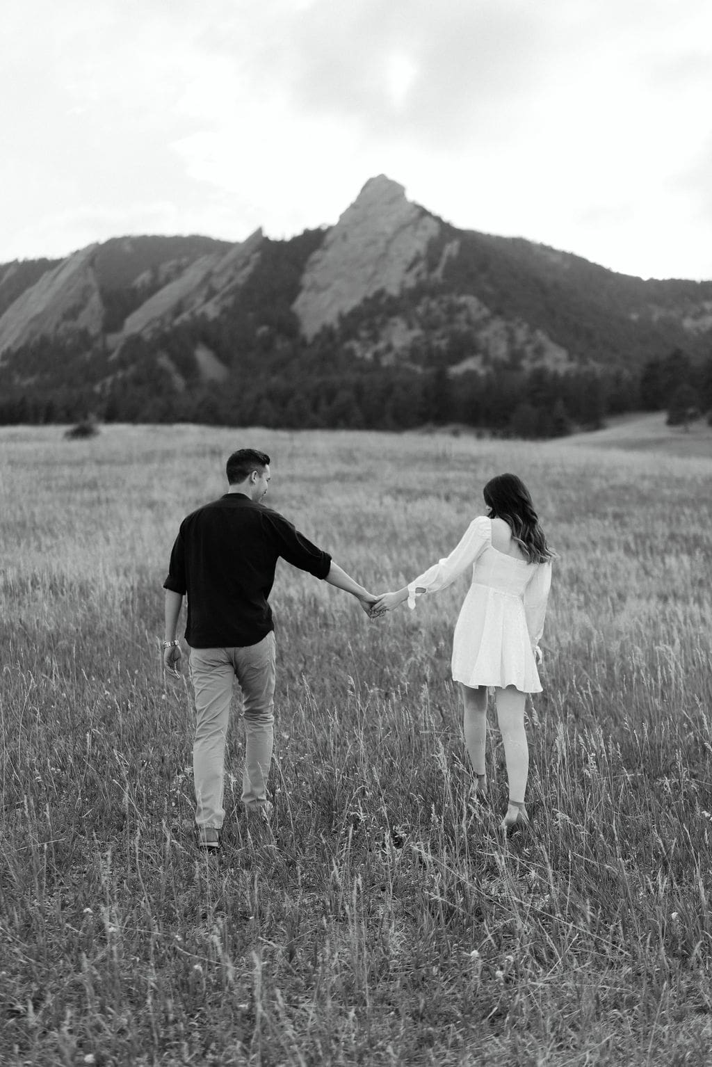 Mountain Engagement photos taken in Boulder Colorado walking through a field at Chautauqua Park hand in hand
