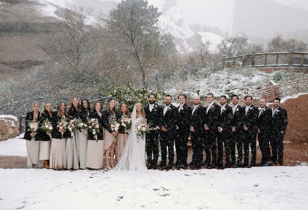 wedding party poses in the snow at red rocks near Denver