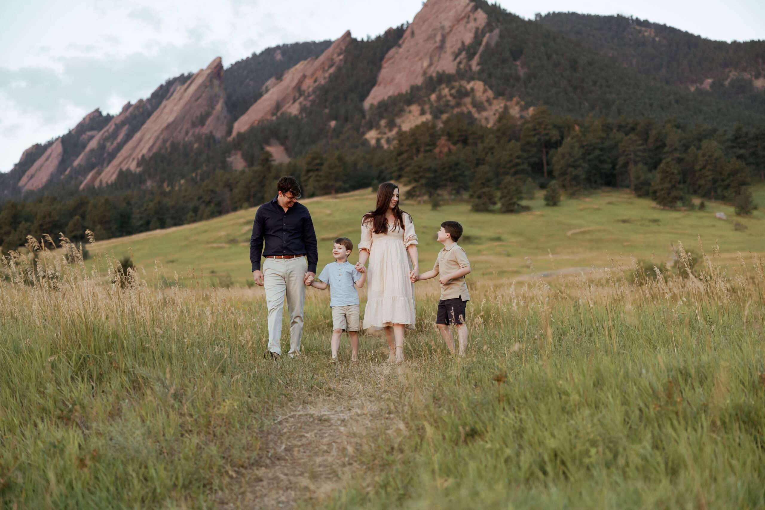 Chautauqua Park Family Photos at Sunrise in front of the flatirons. Family holds hands and walks towards the camera while looking at each other.