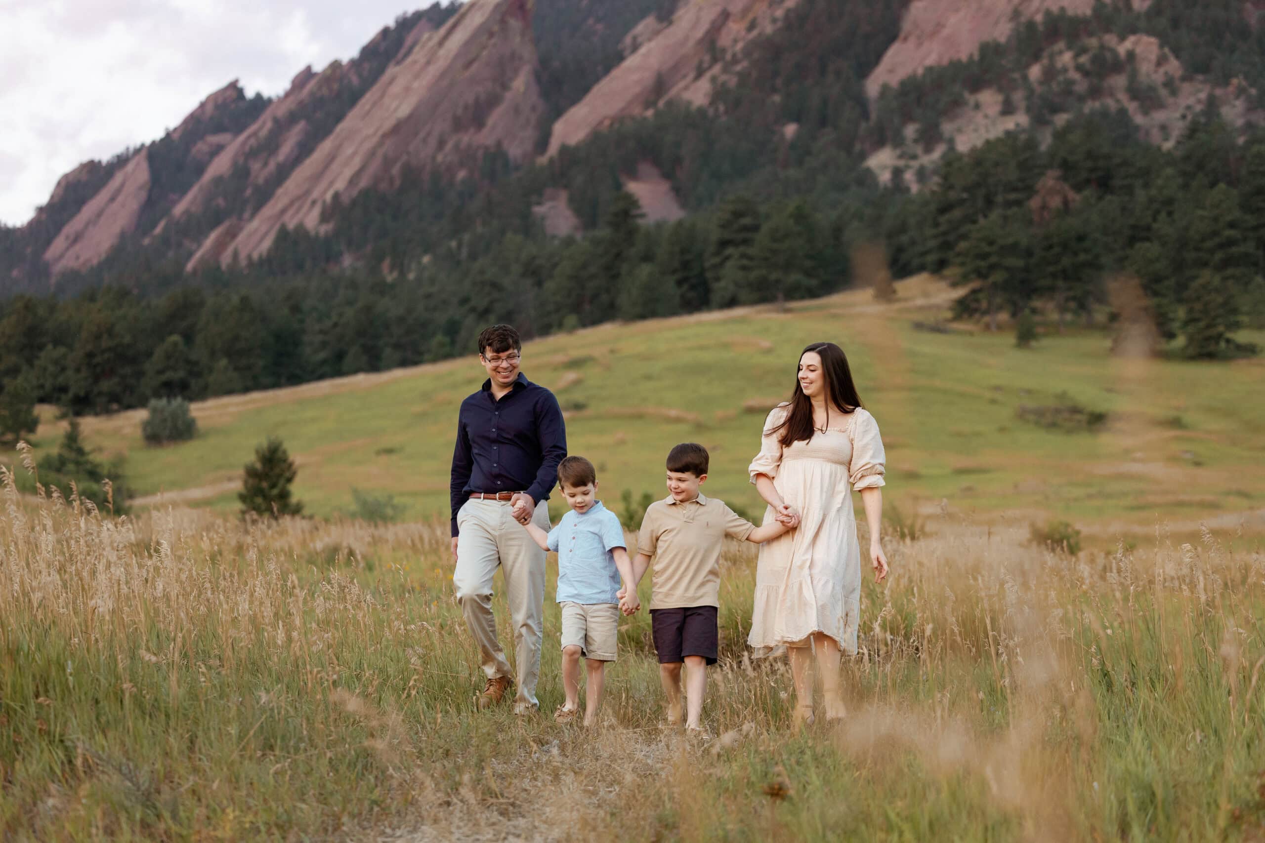 Chautauqua Park Family Photos at Sunrise in front of the flatirons. Family holds hands and walks towards the camera while looking at each other.