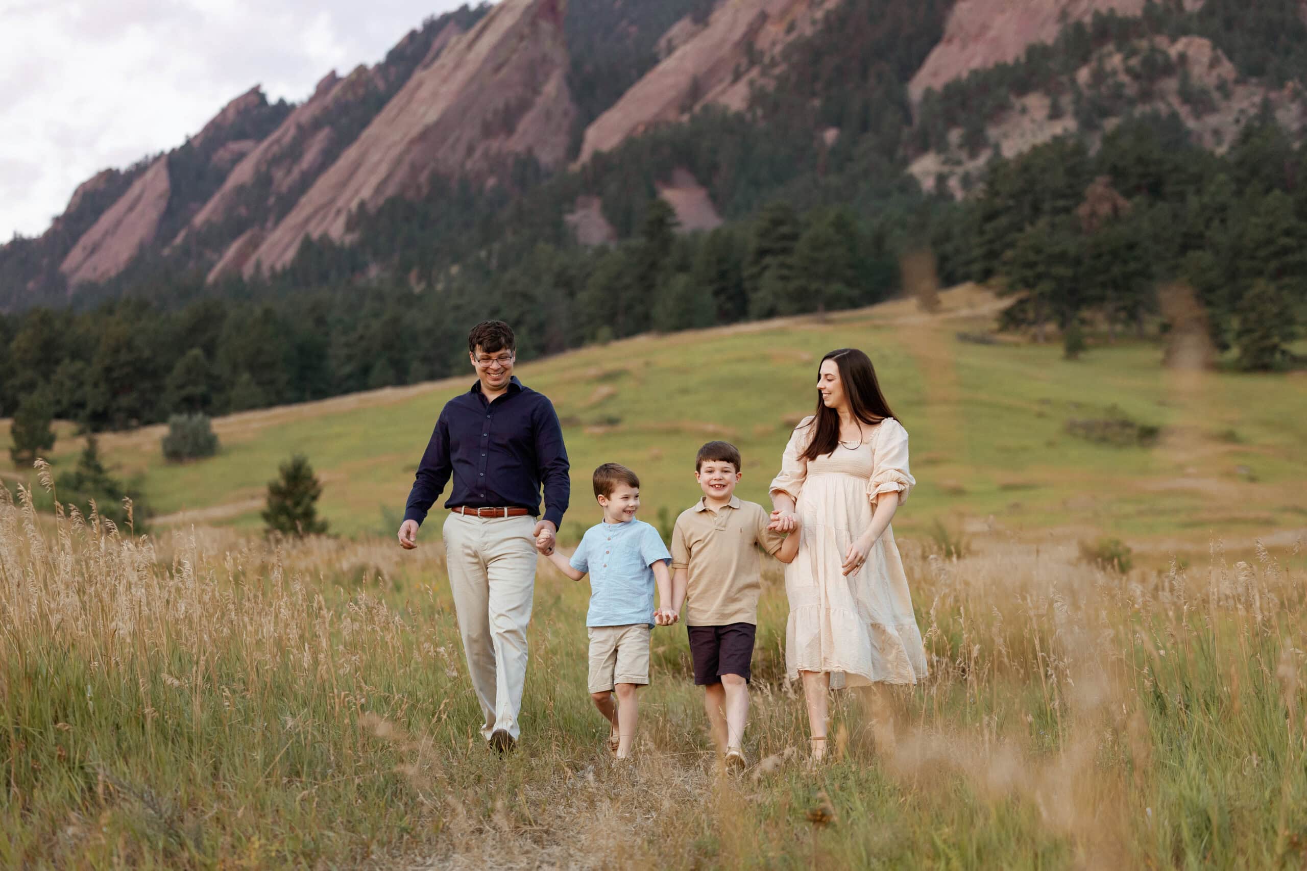 Chautauqua Park Family Photos at Sunrise in front of the flatirons. Family holds hands and walks towards the camera while looking at each other.