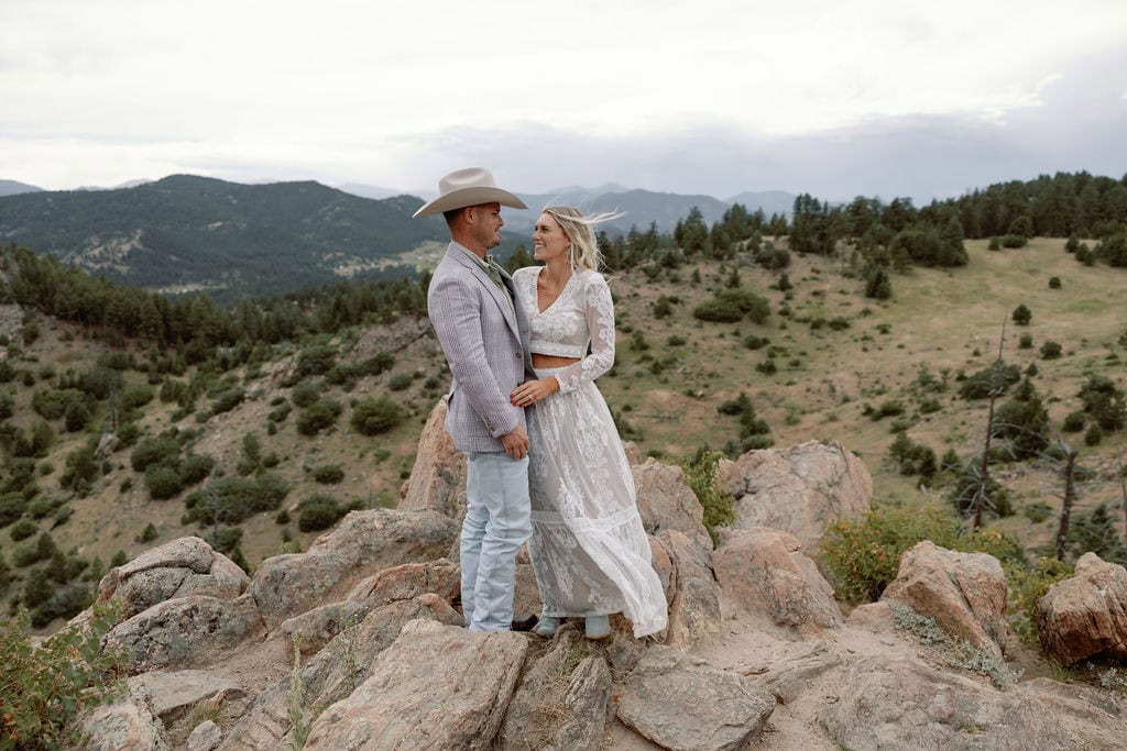 Mount Falcon West Engagement Session with country chic attire and stormy weather. Couple stands at a rocky overlook with windblown hair