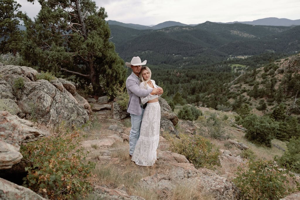 Beautiful couple has a pre-wedding portrait session at mount falcon west on a cloudy july day. They stand together on a rocky ledge overlooking the colorado foothills