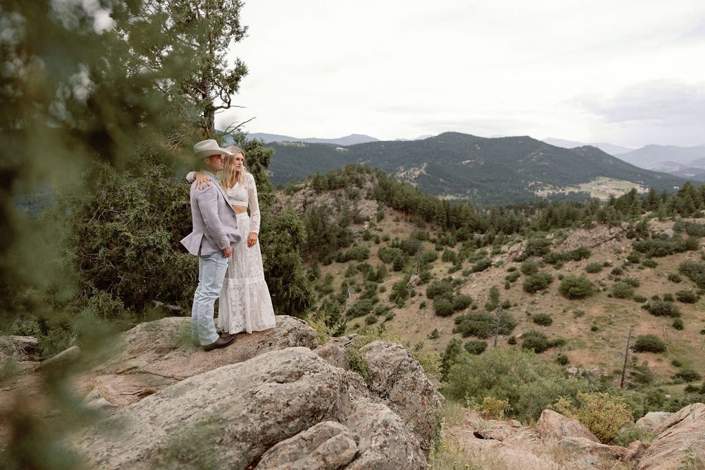 Beautiful couple has a pre-wedding portrait session at mount falcon west on a cloudy july day. They stand together on a rocky ledge overlooking the colorado foothills