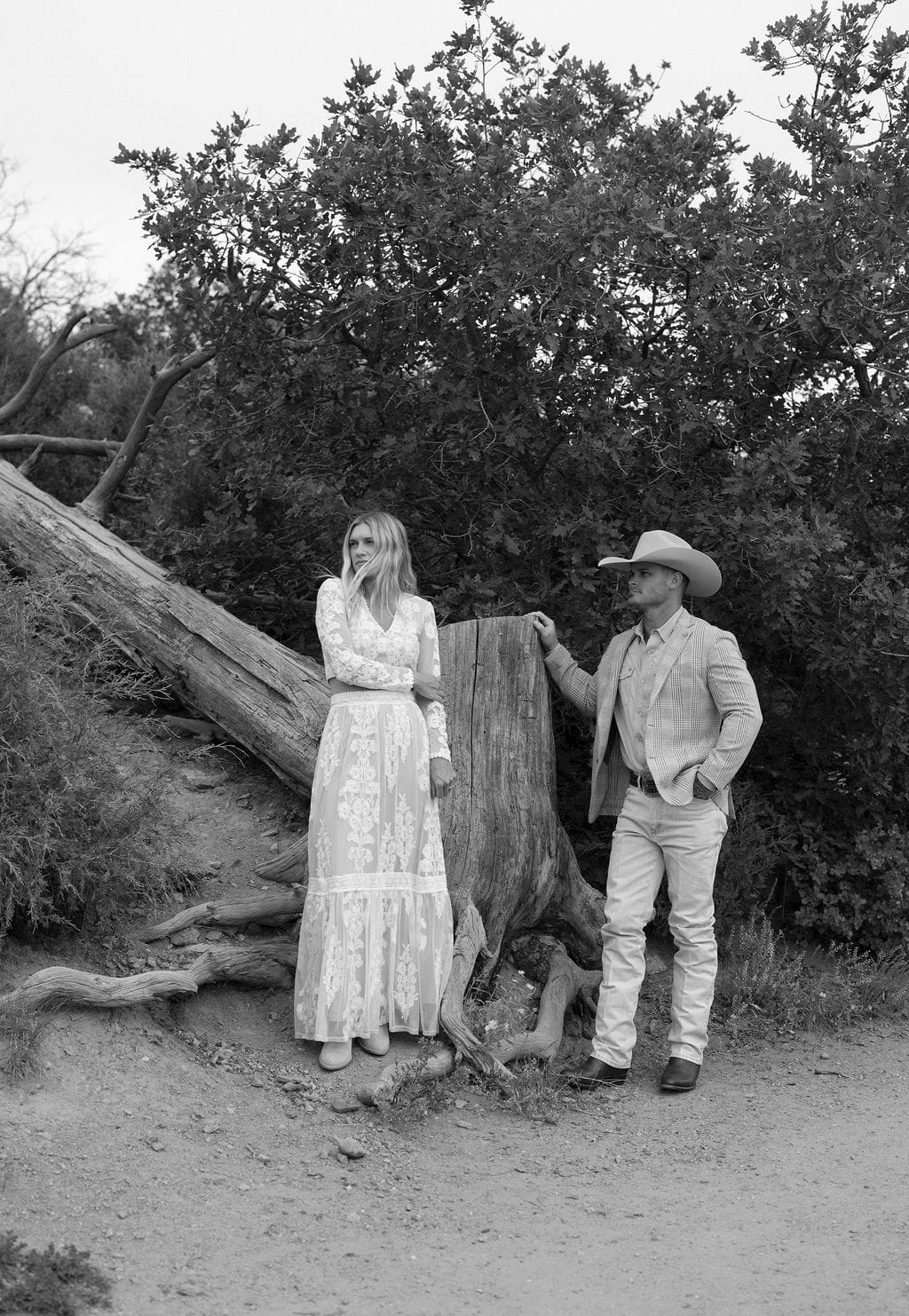 Beautiful couple has an engagement session at mount falcon west on a cloudy july day. They stand together near a giant tree stump. The image is a dramatic black and white photo that looks editorial in nature