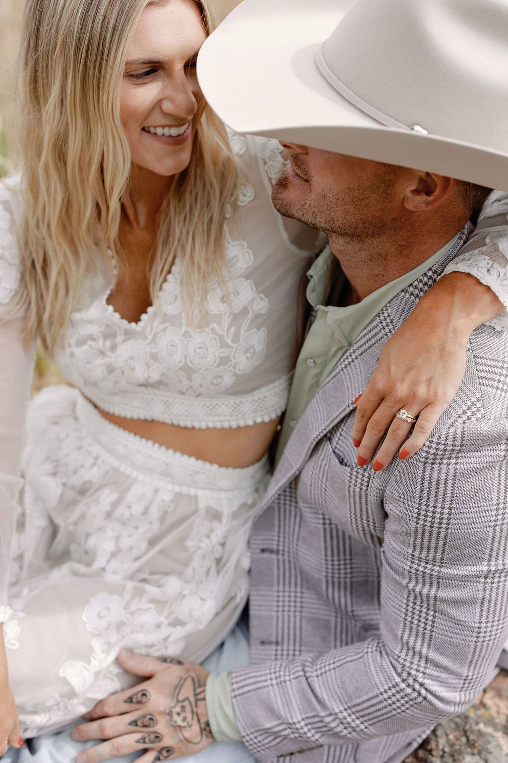 Couple is posed so the woman's hand is showing off her engagement ring, as she sits on her fiance's lap at their mount falcon west engagement session.