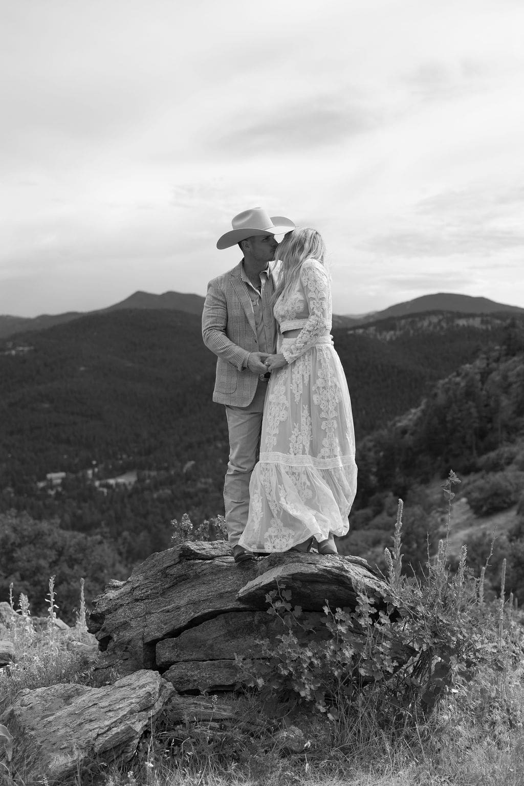 country chic engagement session at mount falcon west on a cloudy July day. A dramatic black and white photo of the couple standing together on a rock with the foothills in the background as they kiss.
