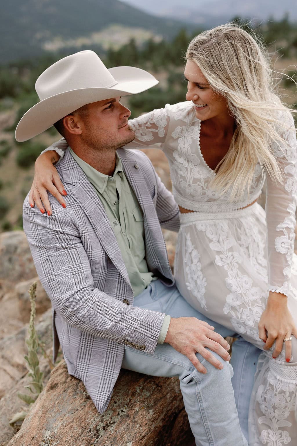 Mount Falcon West Engagement Session with country chic attire and stormy weather. Couple sits at a rocky overlook with windblown hair