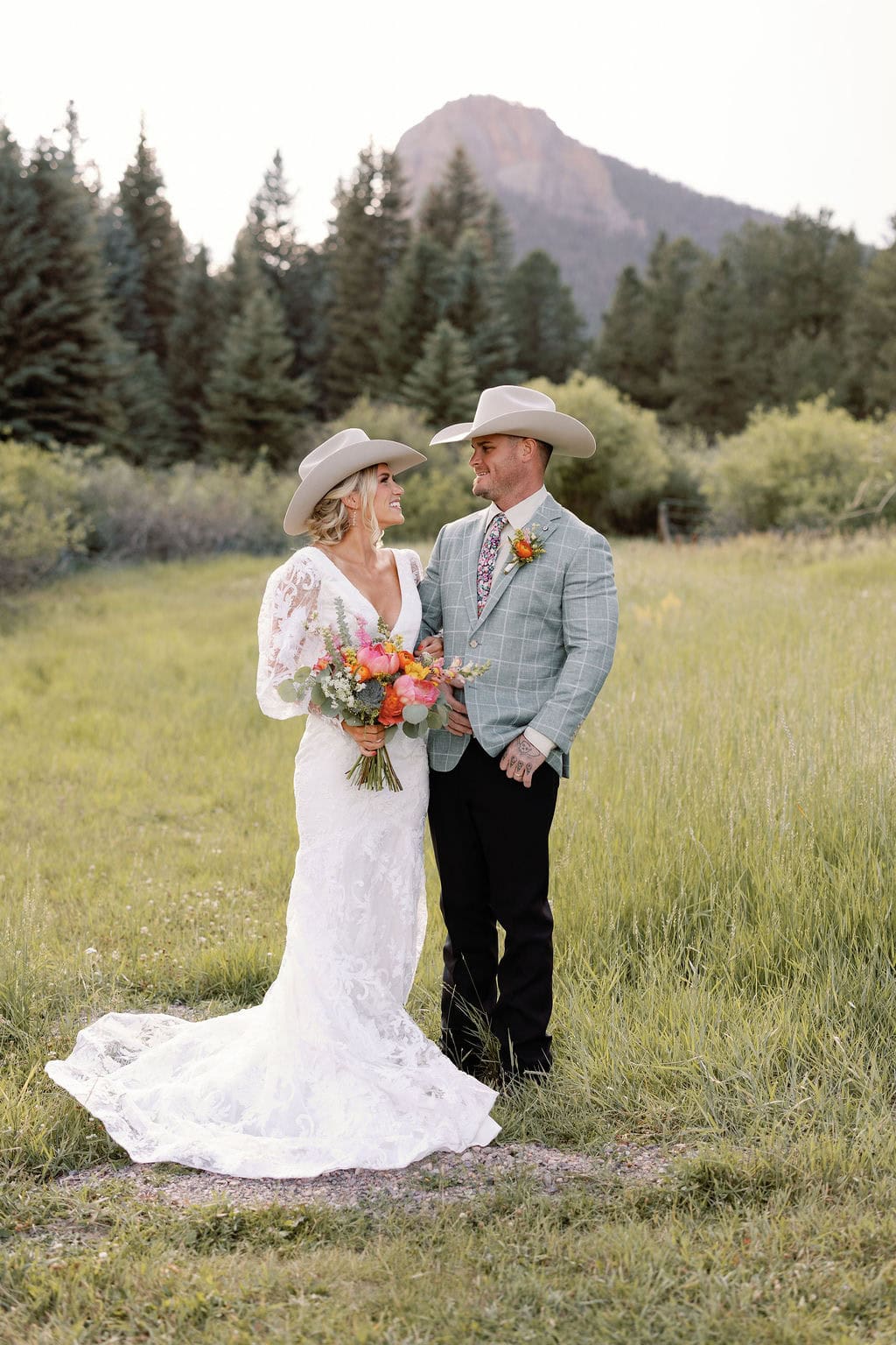 Romantic and chic country mountain wedding portraits in an open field at mountain view ranch by wedgewood weddings. Bride holds colorful floral bouquet and the two look at each other while posing together.