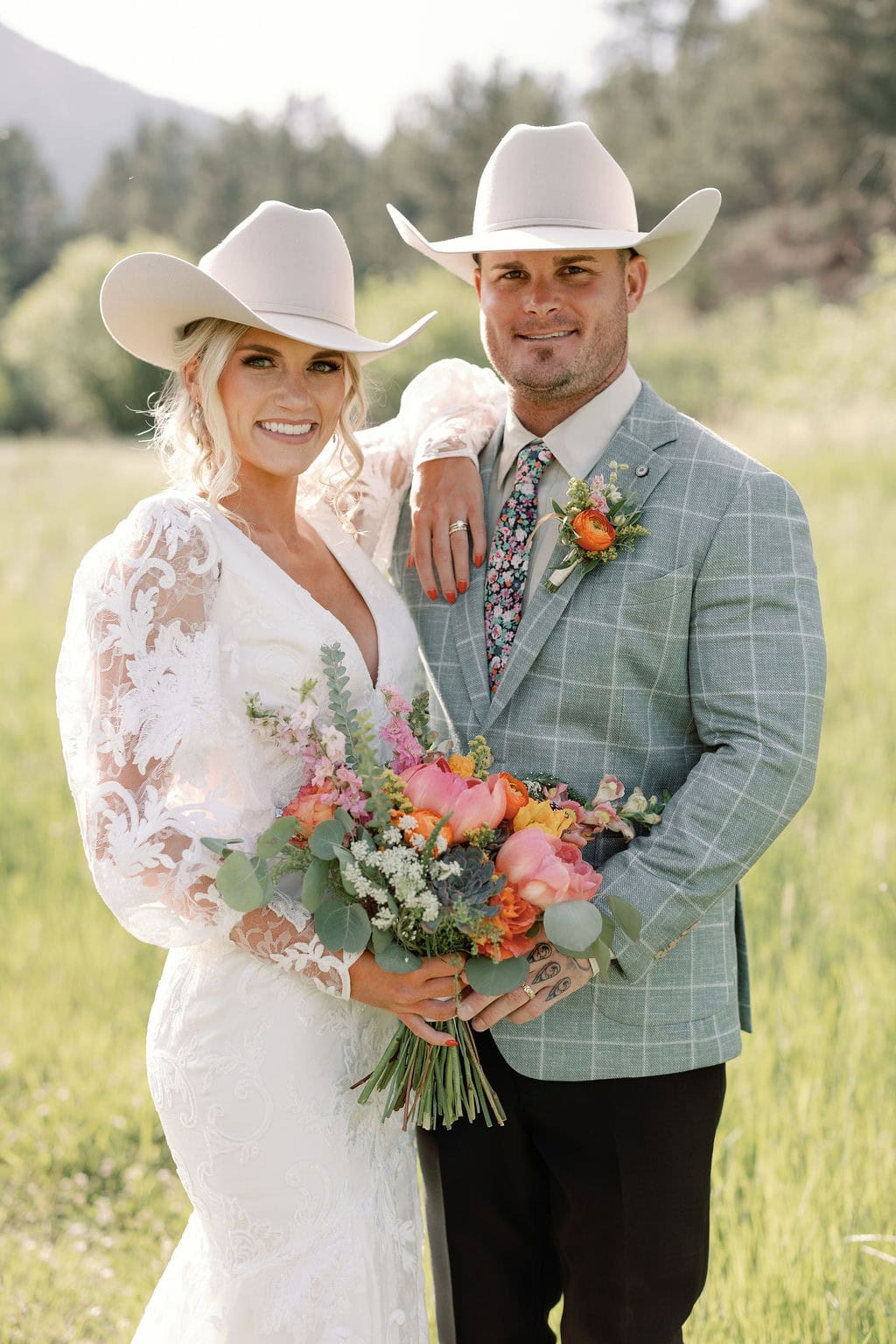 Gorgeous bride and groom portrait in the colorado mountains with country chic wedding attire, cowboy hats, and bright colorful florals