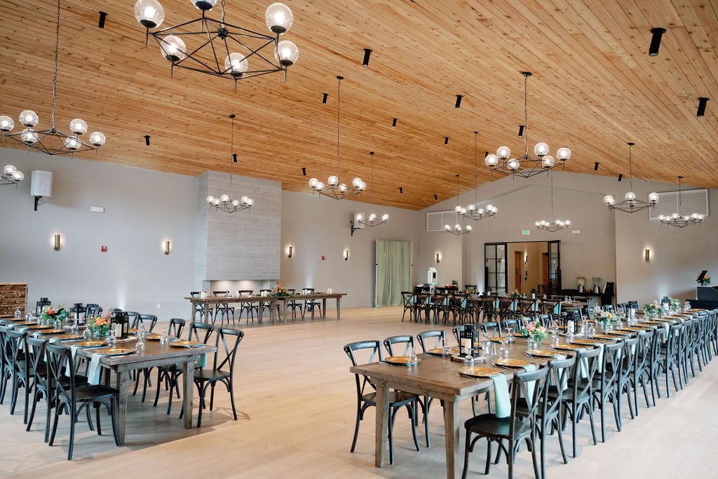 Wide shot of Mountain View Ranch Lakeview Reception Set Up with wooden tables and chairs with a clean and modern chic design utilizing lanterns and florals as centerpieces.
