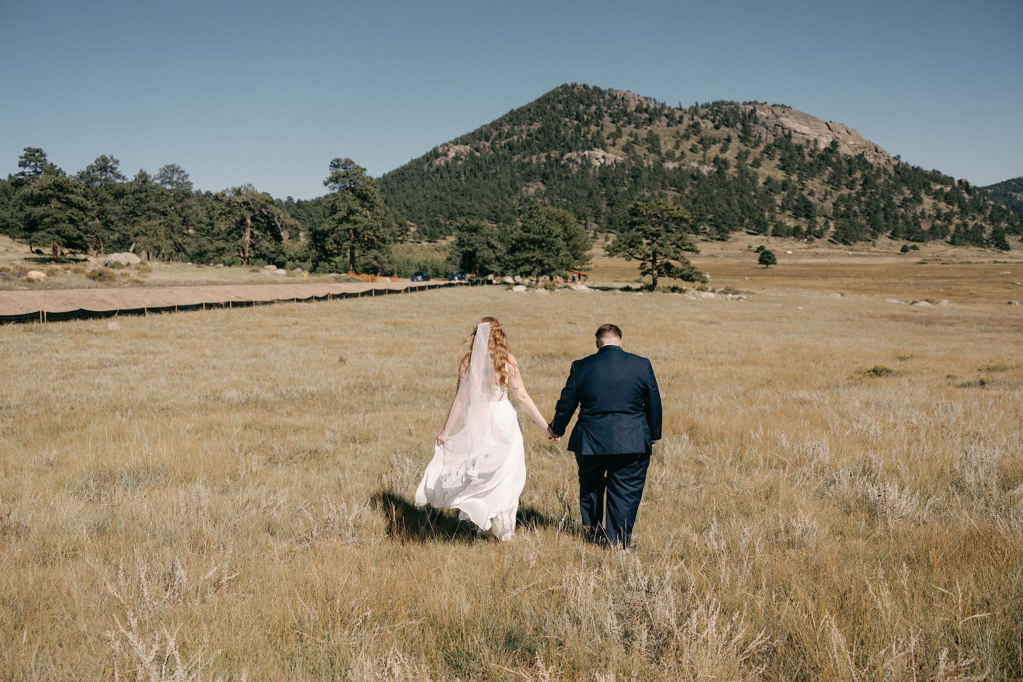 Gorgeous wedding couples portraits in estes park colorado. Rocky mountain national park wedding photography on a bright sunny day. LGBTQ couple walks away from the camera
