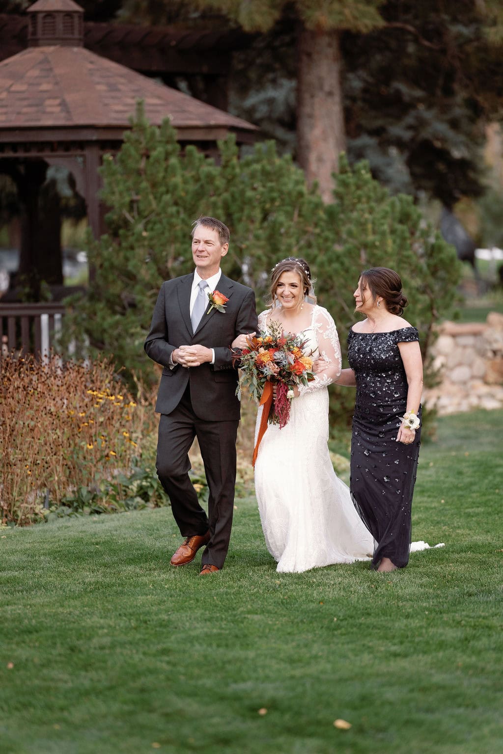 Beautiful fall wedding ceremony, bride walks down with her parents at shupe homestead boulder wedding venue