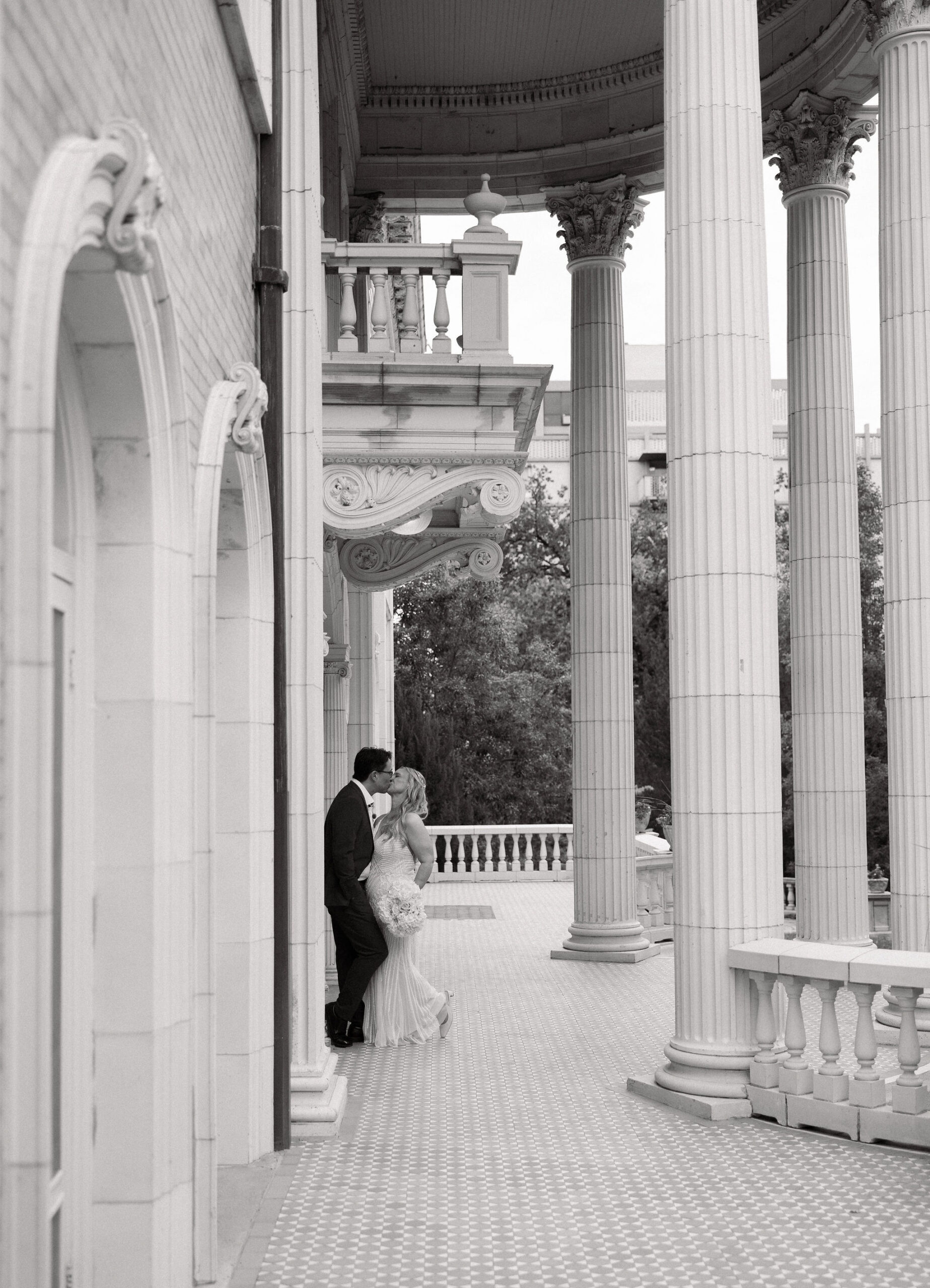 Incredibly romantic black and white photo of bride and groom kissing on the front porch of grant humphrey's mansion on their wedding day.