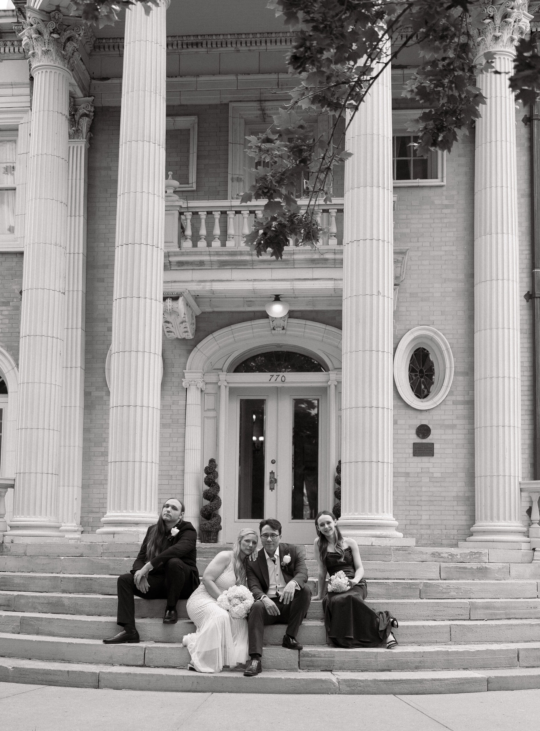 Black and white photo of family on their wedding day sitting on the stairs in front of grant humphrey's mansion